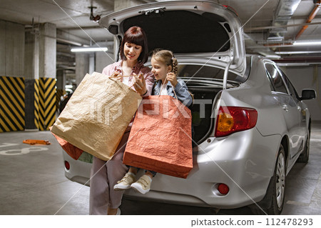 Caucasian family mother and little daughter sitting on open trunk of car. 112478293