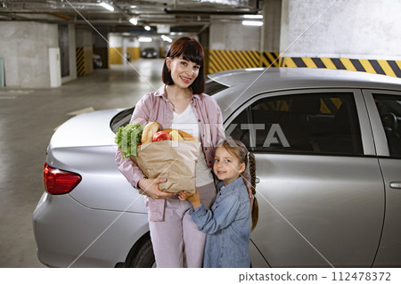 Mother and daughter holding paper bag with fresh vegetables from supermarket. 112478372