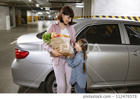 Mother and her little daughter standing beside contemporary vehicle. 112478378