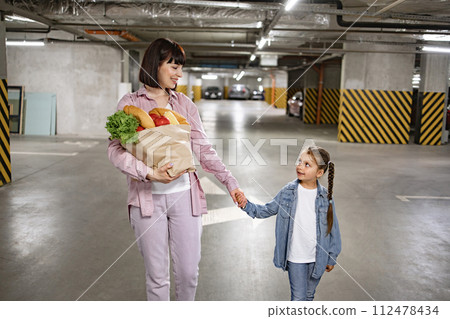 Mother and daughter walking and holding paper bag with vegetables. 112478434