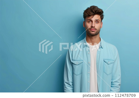 A man in a blue shirt and white shirt is standing in front of a blue wall 112478709