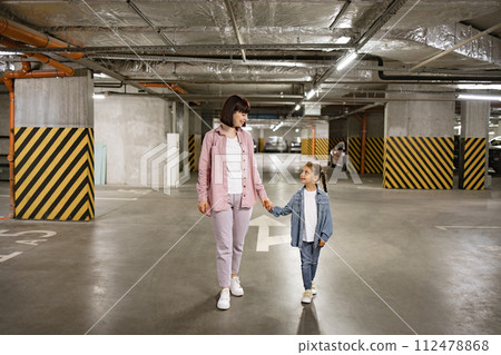 Mother and daughter walking holding hands in modern underground parking Mother and daughter walking holding hands in modern underground parking 112478868