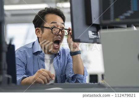 A man in his 50s is surprised when he looks at his computer monitor. 112479021