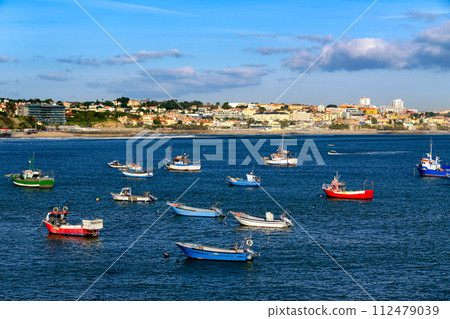 Beautiful view of small fishing boats on sunny day in bay of Cascais, Portugal, quiet and luxurious seaside town near Lisbon with beaches and small port. Clear blue sky, clouds, sunshine, calm ocean 112479039