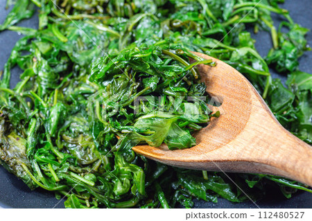 Wilted arugula or rocket salad, preparing a side dish in frying pan, horizontal closeup Wilted arugula or rocket salad, preparing a side dish in frying pan, horizontal closeup 112480527
