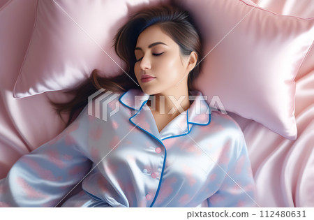 Beautiful young Asian woman sleeping on a bed in pajamas on pink bed linen, romantic shot 112480631