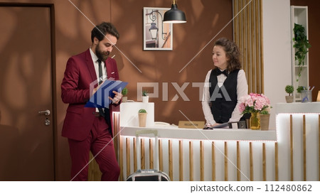 Important guest signing check in forms at reception, arriving at hotel to meet with international associates. Businessman registering in front desk archive log, work trip. Handheld shot. Important guest signing check in forms at reception, arriving at hotel to meet with international associates. Businessman registering in front desk archive log, work trip. Handheld shot. 112480862