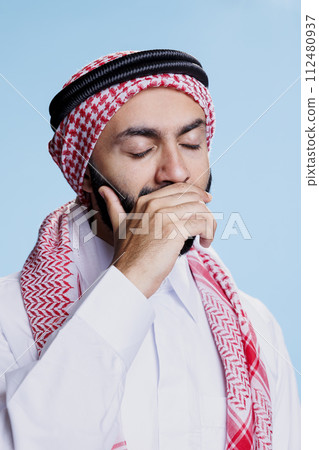 Sleepy man with closed eyes wearing traditional muslim headdress and thobe yawning. Exhausted arab dressed in islamic clothes covering mouth with arm while feeling sleepiness and tiredness Sleepy man with closed eyes wearing traditional muslim headdress and thobe yawning. Exhausted arab dressed in islamic clothes covering mouth with arm while feeling sleepiness and tiredness 112480937