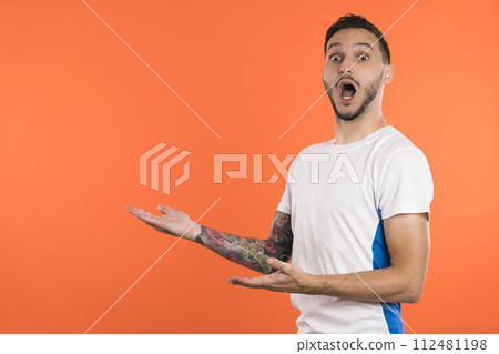 Young male soccer player or fan presenting a product on the side with stretched arms. Copy space 112481198