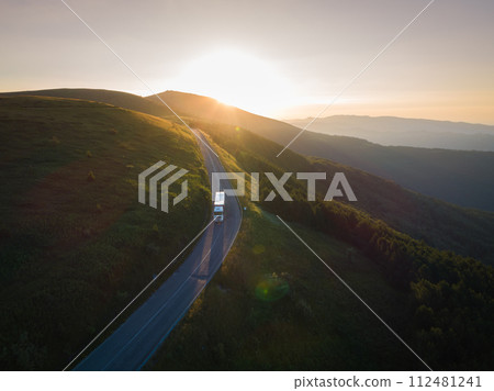 White truck of delivery company with cargo is driving on forest road in the mountains at sunset 112481241