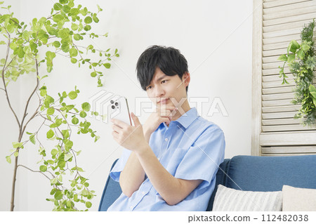 Young man using smartphone while thinking in living room 112482038