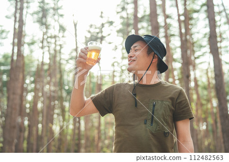 男露營者在露營地喝啤酒(酒精、酒精、精釀啤酒、低麥芽啤酒) 男露營者在露營地喝啤酒(酒精、酒精、精釀啤酒、低麥芽啤酒) 112482563