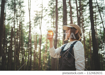 女露營者在露營地喝啤酒(酒精、酒精、精釀啤酒、低麥芽啤酒) 女露營者在露營地喝啤酒(酒精、酒精、精釀啤酒、低麥芽啤酒) 112482631