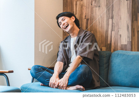 Young Asian/Japanese man laughing out loud while watching TV/videos/videos in his living room (relaxed) Young Asian/Japanese man laughing out loud while watching TV/videos/videos in his living room (relaxed) 112483053