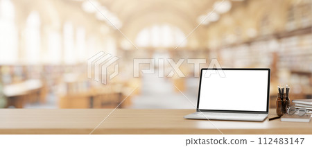 A laptop computer mockup on a wooden desk with a blurred background of a beautiful spacious library. A laptop computer mockup on a wooden desk with a blurred background of a beautiful spacious library. 112483147