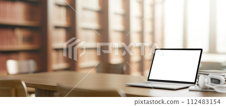 A white-screen laptop computer mockup on a wooden table in a library. A white-screen laptop computer mockup on a wooden table in a library. 112483154
