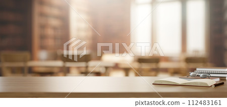 A wooden table features books, eyeglasses, and a presentation space in a library. A wooden table features books, eyeglasses, and a presentation space in a library. 112483161