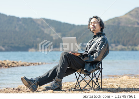 A man in his 30s working remotely by the lake A man in his 30s working remotely by the lake 112487661