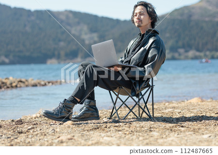 A man in his 30s working remotely by the lake 112487665