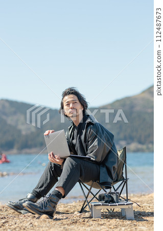 A man in his 30s working remotely by the lake A man in his 30s working remotely by the lake 112487673