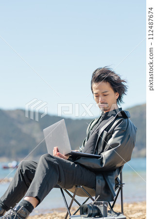 A man in his 30s working remotely by the lake A man in his 30s working remotely by the lake 112487674