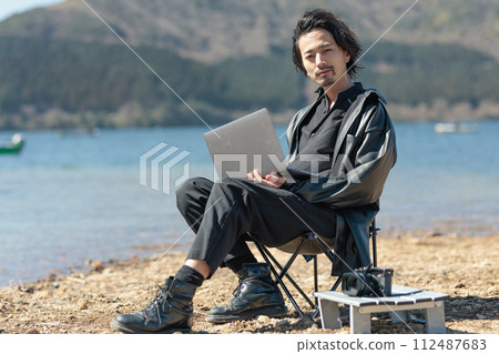 A man in his 30s working remotely by the lake 112487683