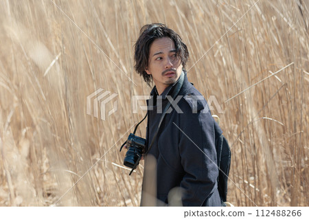 A man in his 30s holding a camera in front of pampas grass A man in his 30s holding a camera in front of pampas grass 112488266