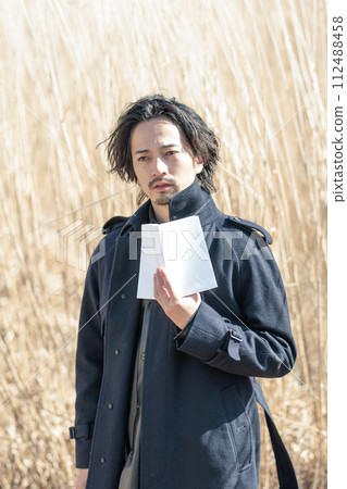 A man in his 30s holding a book in front of pampas grass 112488458