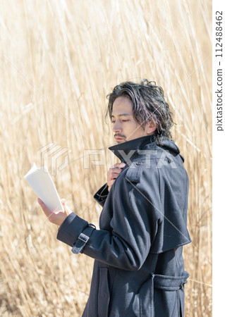 A man in his 30s holding a book in front of pampas grass 112488462