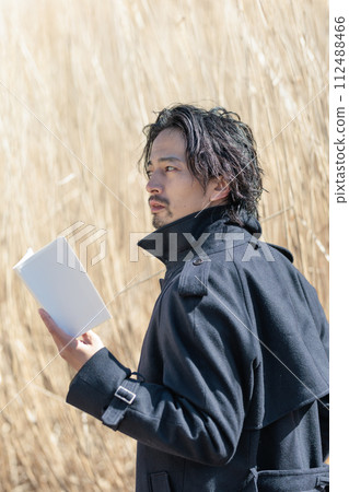 A man in his 30s holding a book in front of pampas grass 112488466