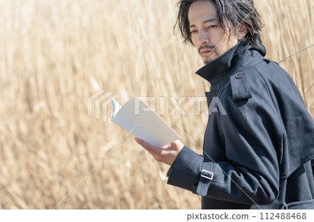 A man in his 30s holding a book in front of pampas grass 112488468