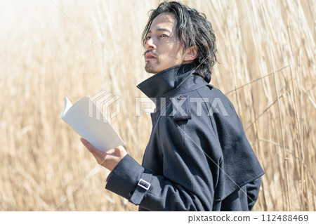 A man in his 30s holding a book in front of pampas grass 112488469