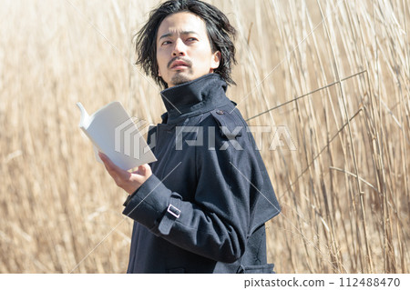 A man in his 30s holding a book in front of pampas grass 112488470