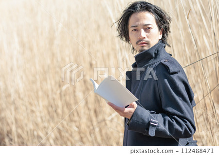 A man in his 30s holding a book in front of pampas grass A man in his 30s holding a book in front of pampas grass 112488471
