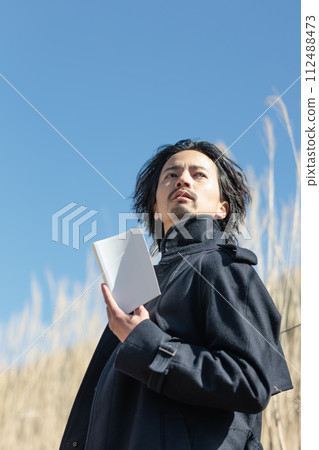 一名30多歲的男子在蒲葦前拿著一本書 一名30多歲的男子在蒲葦前拿著一本書 112488473