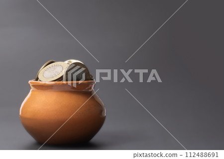 Coins in a clay pot on a gray background with copy space. Coins in a clay pot on a gray background with copy space. 112488691