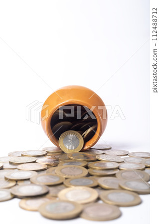 Indian coins spilling out of a clay pot isolated on white background. 112488712