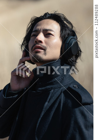 A man in his 30s listening to music in a grassy field A man in his 30s listening to music in a grassy field 112489288