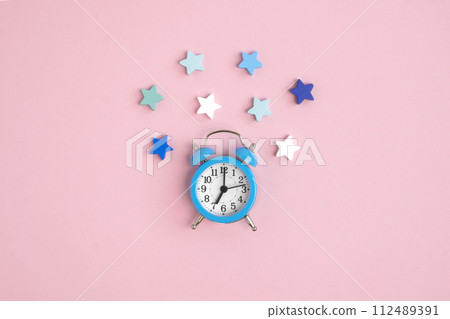 Blue alarm clock on a pink background, decorated with white, blue and green stars around. Bedtime concept, Christmas composition, insomnia, reminder, starfall, romantic date.place for logo. Copyspace Blue alarm clock on a pink background, decorated with white, blue and green stars around. Bedtime concept, Christmas composition, insomnia, reminder, starfall, romantic date.place for logo. Copyspace 112489391
