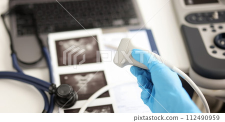 Doctor holding ultrasound probe against background of pictures and medical documents closeup Doctor holding ultrasound probe against background of pictures and medical documents closeup 112490959