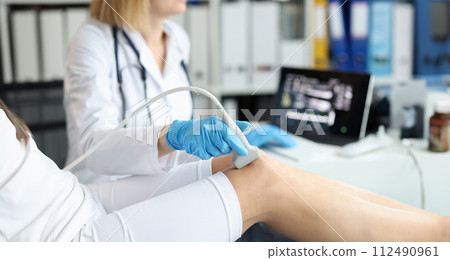 Doctor doing ultrasound examination of patient knee joint in clinic closeup 112490961