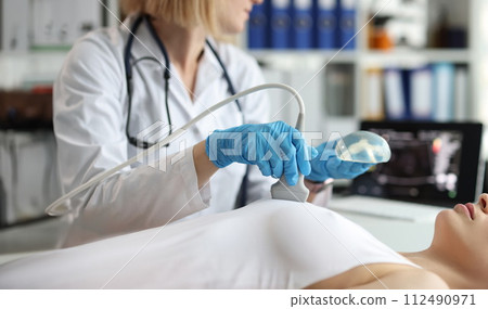 Doctor holding implant and doing ultrasound examination of woman breasts closeup 112490971
