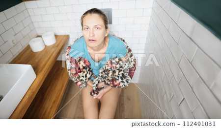 Young woman sitting on toilet and grimacing Young woman sitting on toilet and grimacing 112491031