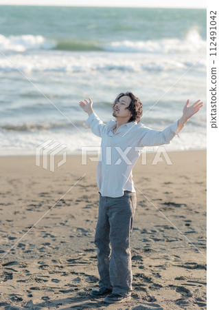 A man in his 30s wearing a white shirt standing by the seaside A man in his 30s wearing a white shirt standing by the seaside 112491042