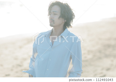 A man in his 30s wearing a white shirt standing by the seaside A man in his 30s wearing a white shirt standing by the seaside 112491043