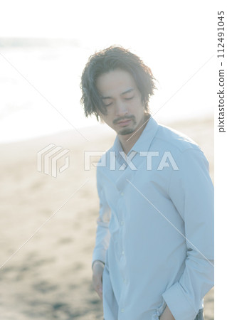 一名30多歲的男子穿著白襯衫站在海邊 112491045