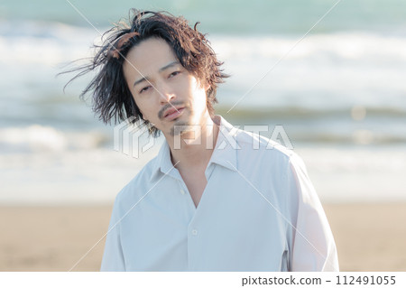 A man in his 30s wearing a white shirt standing by the seaside 112491055