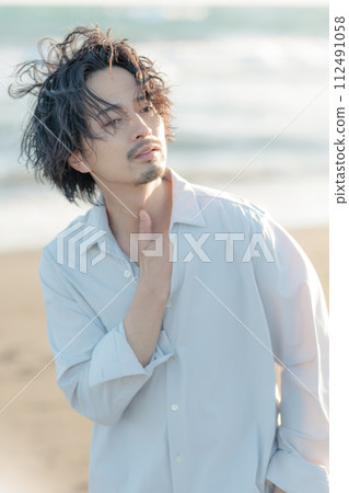 A man in his 30s wearing a white shirt standing by the seaside 112491058