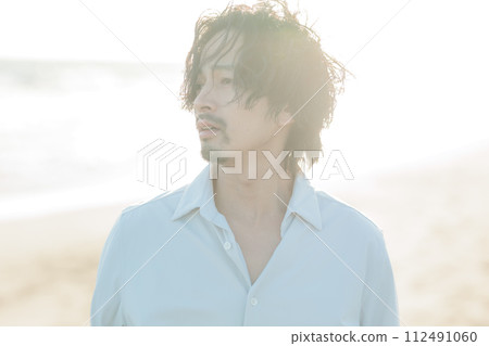 A man in his 30s wearing a white shirt standing by the seaside 112491060