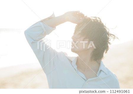 A man in his 30s wearing a white shirt standing by the seaside 112491061